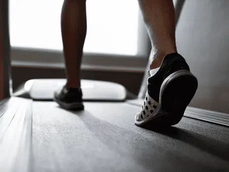 Close-up of a person's foot in a black and white sneaker walking on a treadmill.