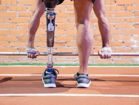 Athlete with a prosthetic leg preparing to lift a barbell on a track surface.