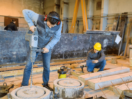 Construction worker using a jackhammer on a concrete block inside an industrial site
